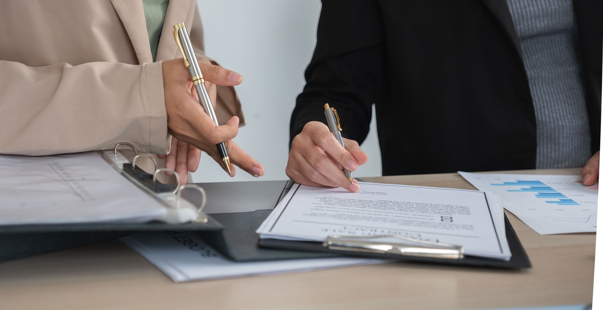 Two businesswomen sign a business contract together, drafting a company contract document.